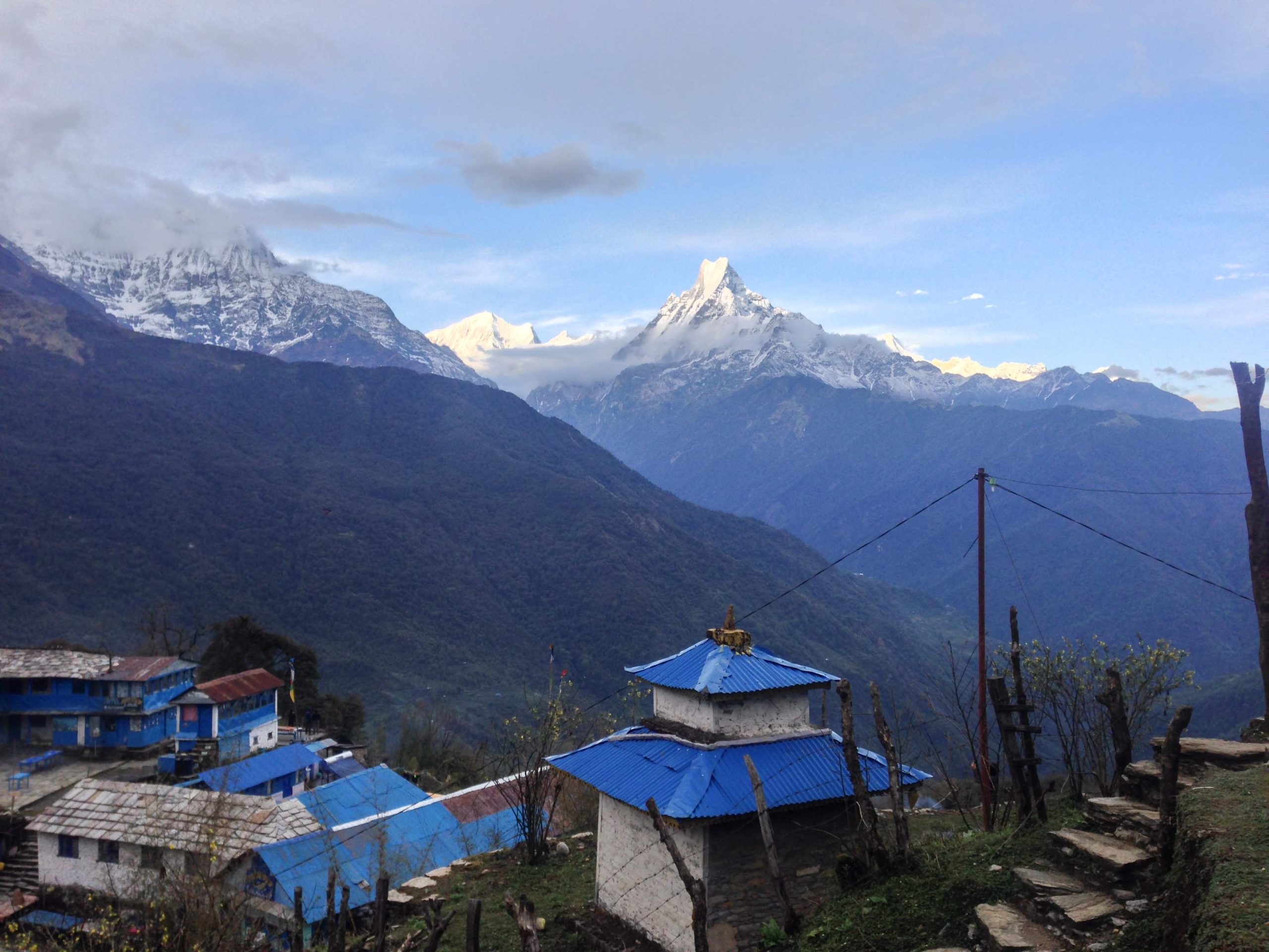 a blue buildings with a blue roof and a snowy mountain range - Annapurna Base Camp Trek 